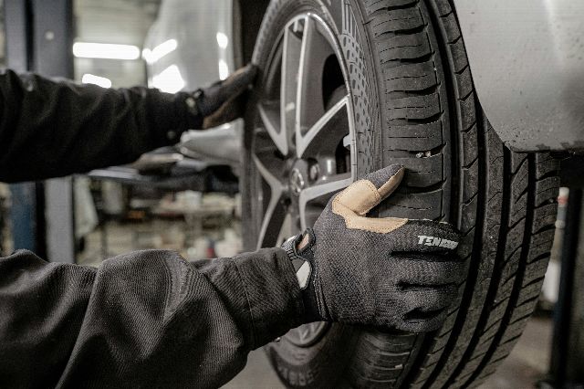 A mechanic's gloved hands on a car tyre